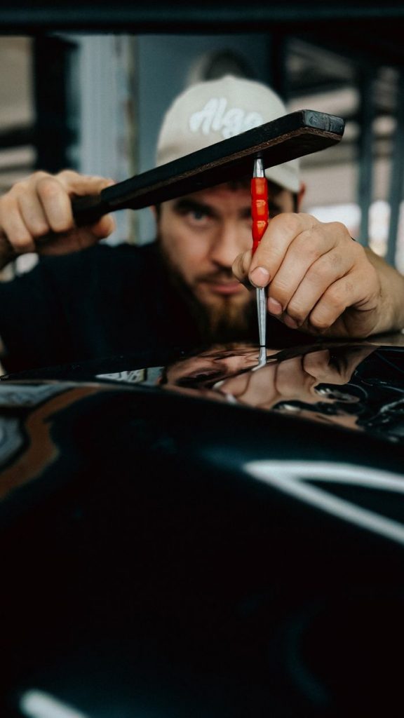 Mechanic expertly repairing car dent using specialized tool in workshop.