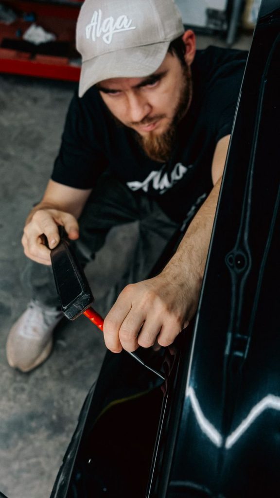 Mechanic uses tools to repair a car, showcasing hands-on automotive work indoors.